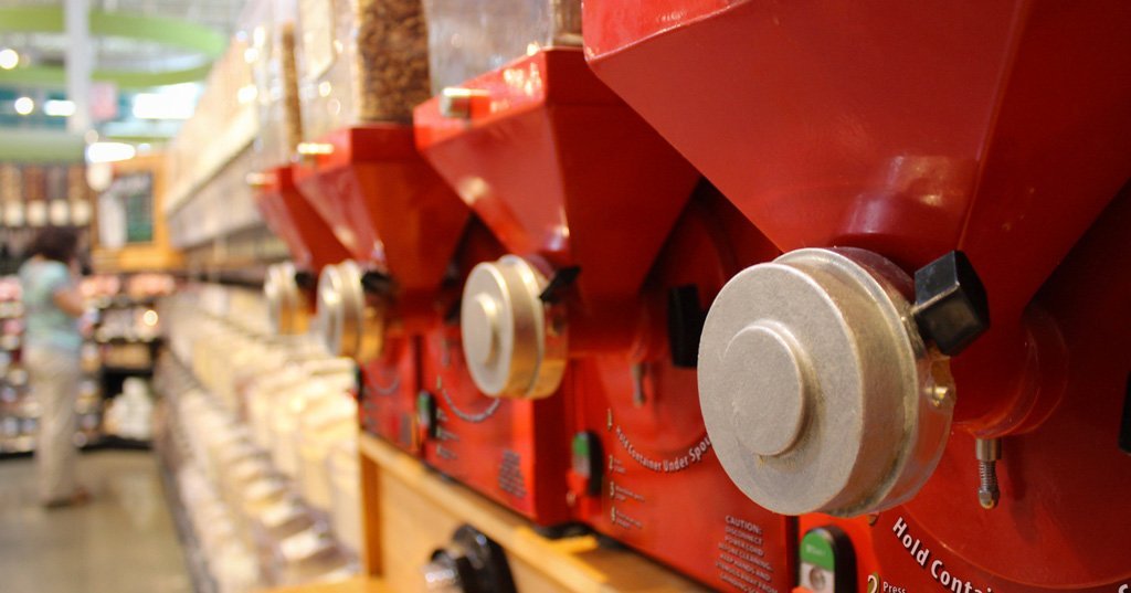A close-up image of the dispenser piece of one of four nut butter grinders, lined up beside one another.